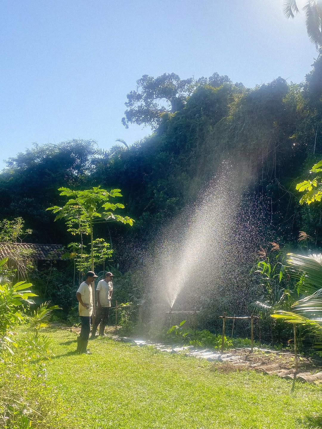Duas pessoas no jardim com irrigacao e mata ao fundo no Sitio Labareda