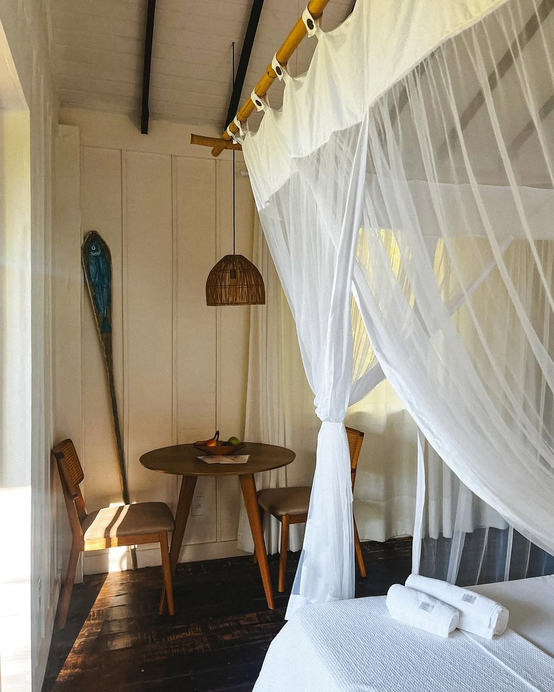 Cama com dossel branco, luminaria artesanal e mesa com frutas