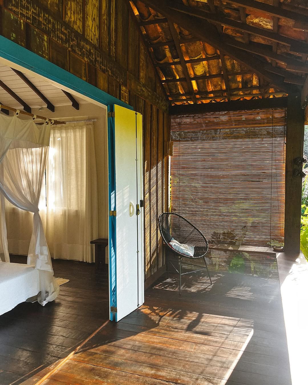 Quarto rustico com cortinas brancas e varanda com cadeira no Sitio Labareda
